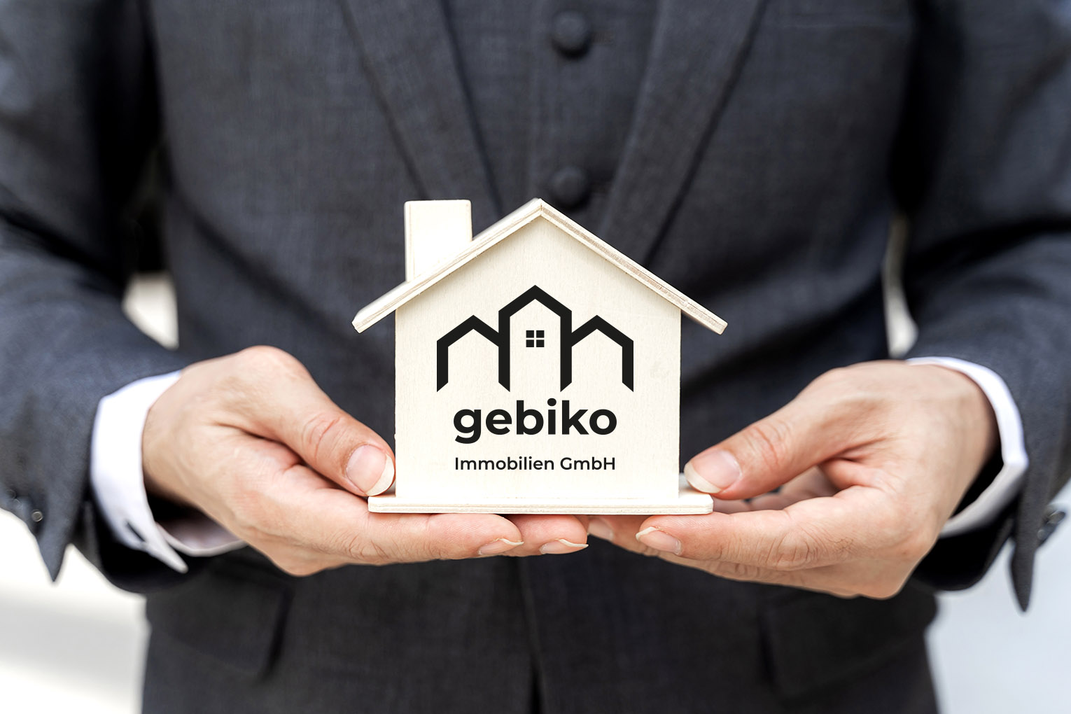 Geschäftsmann hältModell eines Hauses mit gebiko Immobilien GmbH Logo